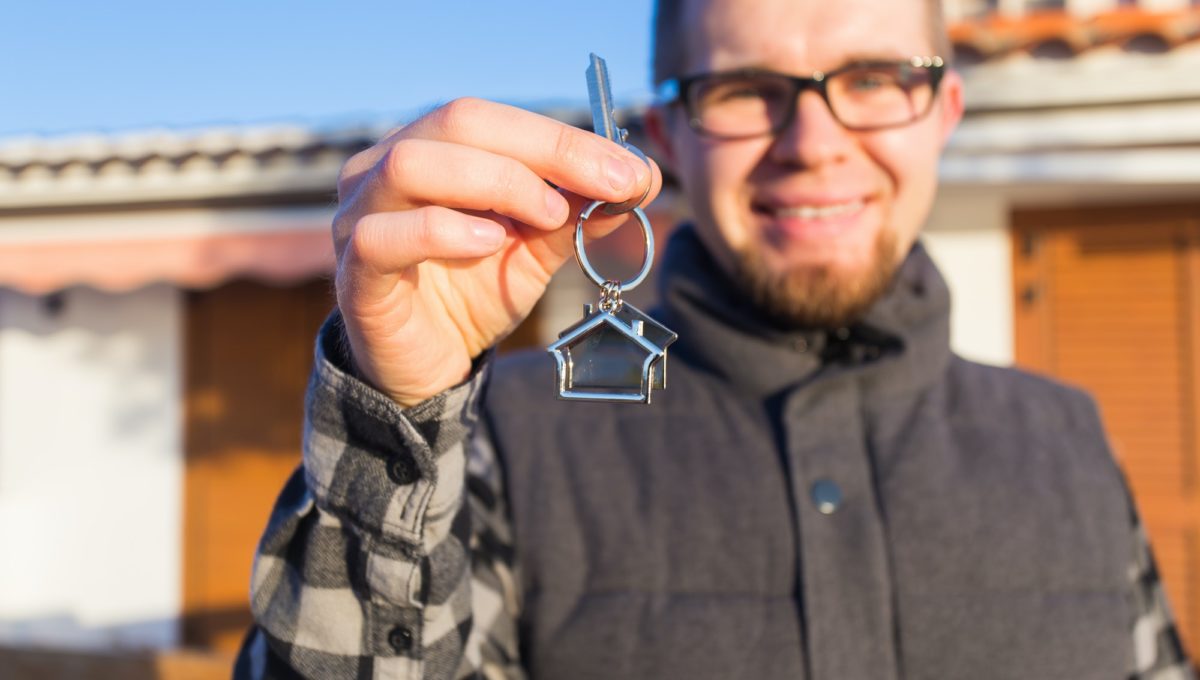 Dwelling, buying home, real estate and ownership concept - handsome man showing his key to new home