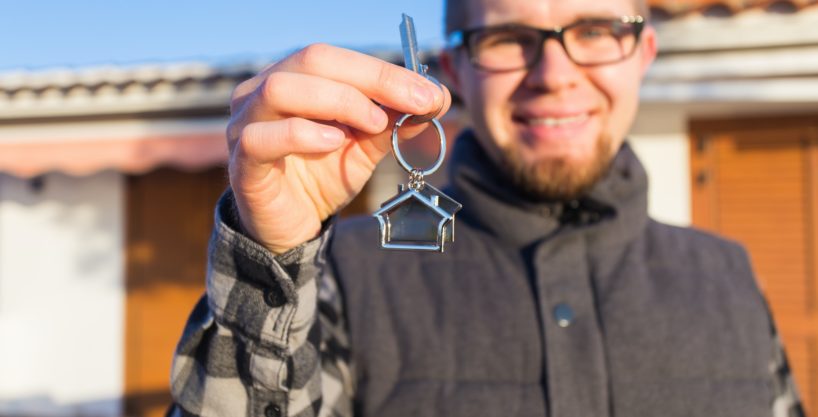 Dwelling, buying home, real estate and ownership concept - handsome man showing his key to new home