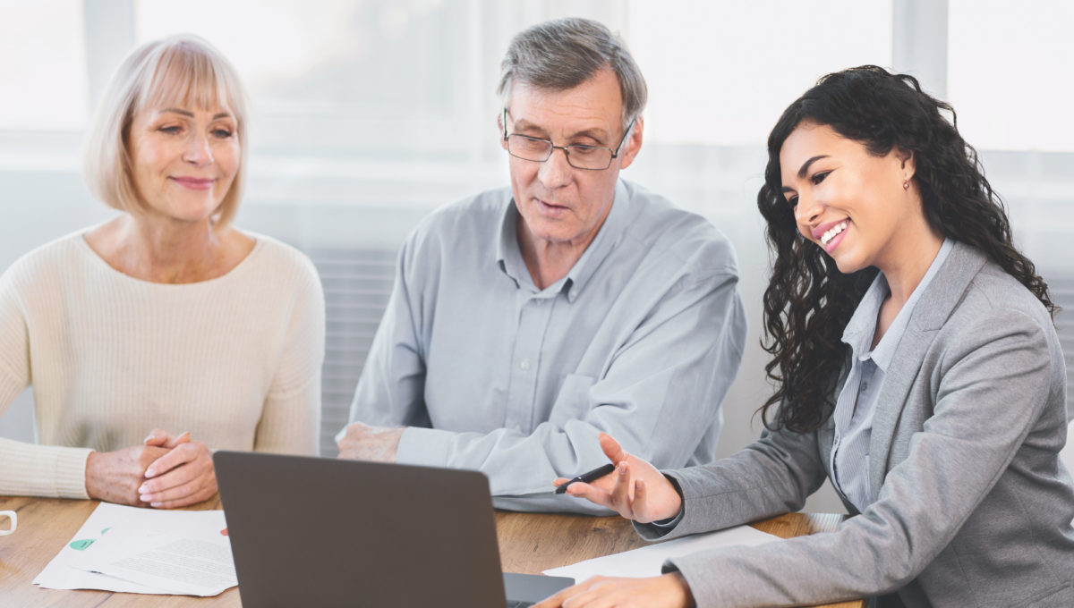 Real Deal. Older couple considering new home purchase talking with estate agent who showing them laptop